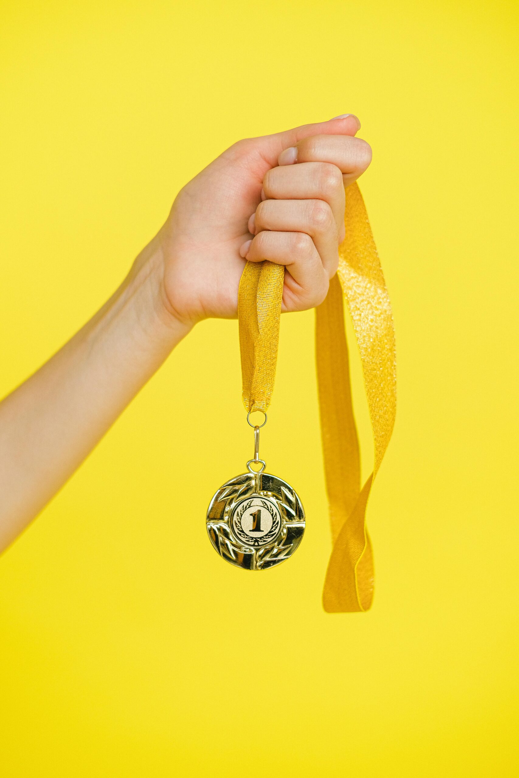 Close-up of a hand holding a gold medal symbolizing achievement and success.