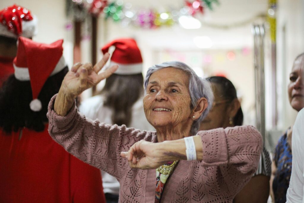 Projetos Joyful elderly woman celebrating indoors during a festive Christmas event.