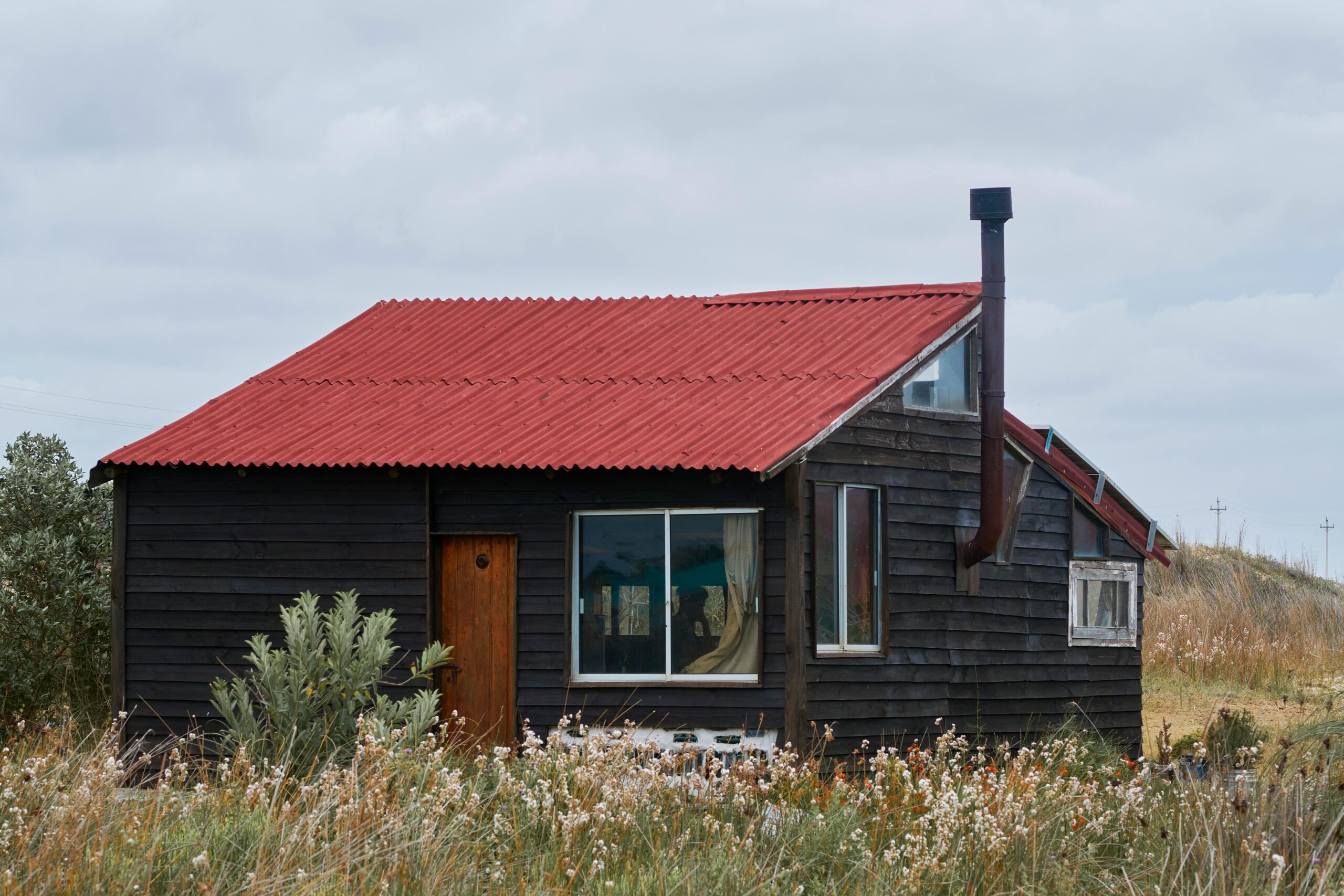 Charming wooden cabin with a vibrant red roof set in a serene natural landscape.