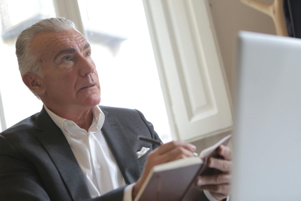 Senior businessman in formal attire writing notes while sitting at a desk in an office.